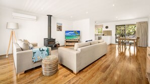 A modern living room with a fireplace, a television, and a dining area with a view of the outdoors. - Clifden Cottage in Cowes (Cowes)