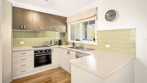 A modern kitchen with wooden cabinets, a built-in oven, a sink, and a window with a view. - Clifden Cottage in Cowes (Cowes)
