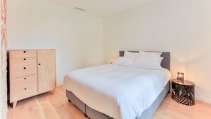 Een slaapkamer met een bed, een houten kast en een rond nachtkastje met een lamp.