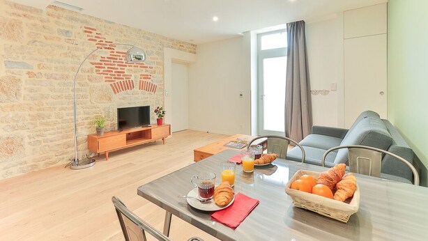 Een moderne woonkamer met een bakstenen muur, een flatscreen televisie, een houten salontafel en een ontbijt klaargemaakte eethoek.