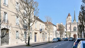 Een straat met historische gebouwen, een kerk met een hoge spits en geparkeerde auto's.