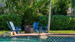 A pool area with blue Adirondack chairs, a small wooden table, and a tiled pool edge. - ⚓Private pool home-Boat Dock-Arcade Games!⚓🌅 (Bradenton)