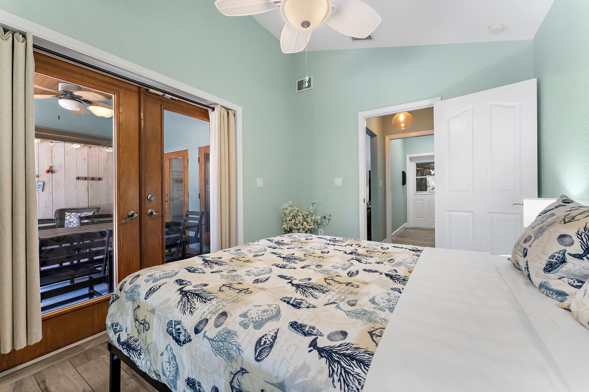 Une chambre à coucher comprenant un lit, un ventilateur de plafond, une armoire en bois et une porte donnant sur une salle de bain.