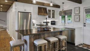A modern kitchen with white cabinetry, a wooden island with bar stools, stainless steel appliances, and pendant lighting. - High Noon: Modern Mountaintop Home w 2 Covered Porches, Firepit | Pet Friendly (Highlands)
