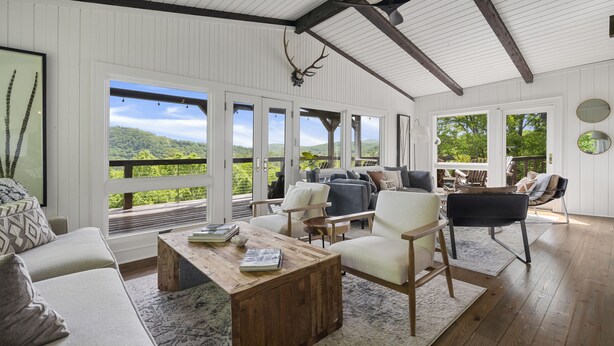 A spacious living area with a large window overlooking a lush landscape, furnished with a sofa, chairs, and a coffee table. - High Noon: Modern Mountaintop Home w 2 Covered Porches, Firepit | Pet Friendly (Highlands)