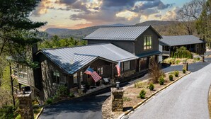 A two-story lodge with a stone facade, a metal roof, and American flags. - High Noon: Modern Mountaintop Home w 2 Covered Porches, Firepit | Pet Friendly (Highlands)