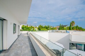 A modern building with a covered outdoor area, a glass railing, and a view of greenery and other buildings in the distance. - Casa Blanca Magnificent Villa With Modern Design, walking distance to beach (Carvoeiro)