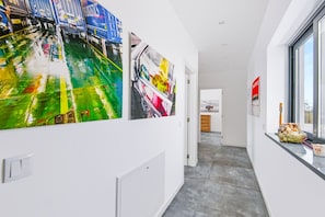 A hallway with a view to a kitchen and dining area, featuring artwork on the walls and a window with a view.