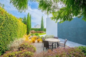 A modern outdoor patio with a round table and chairs, surrounded by well-maintained hedges and a variety of plants. - Casa Blanca Magnificent Villa With Modern Design, walking distance to beach (Carvoeiro)