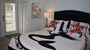 A bedroom with a bed, a door, a wall with a framed quote, a nightstand with a lamp, and a sign. - "Salty Siren" Mermaid Themed Room at Weeki Wachee Waterfront Adventure Retreat (Weeki Wachee)