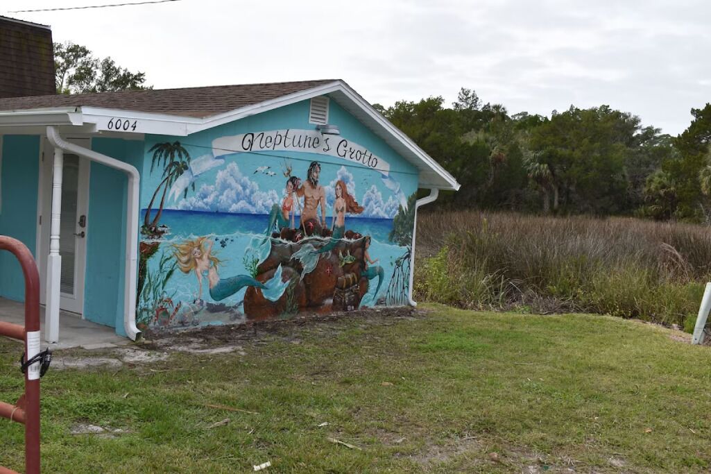 Un edificio con un mural de sirenas y un letrero que dice 'Neptune's Grotto'.