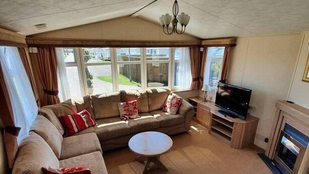 A cozy living room with a sectional sofa, a round coffee table, a flat-screen TV, and a fireplace. - Caravan -chapel, Skegness With Decking From March (Skegness)