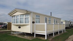 A single-story mobile home with a white exterior and a fenced porch area. - Caravan -chapel, Skegness With Decking From March (Skegness)