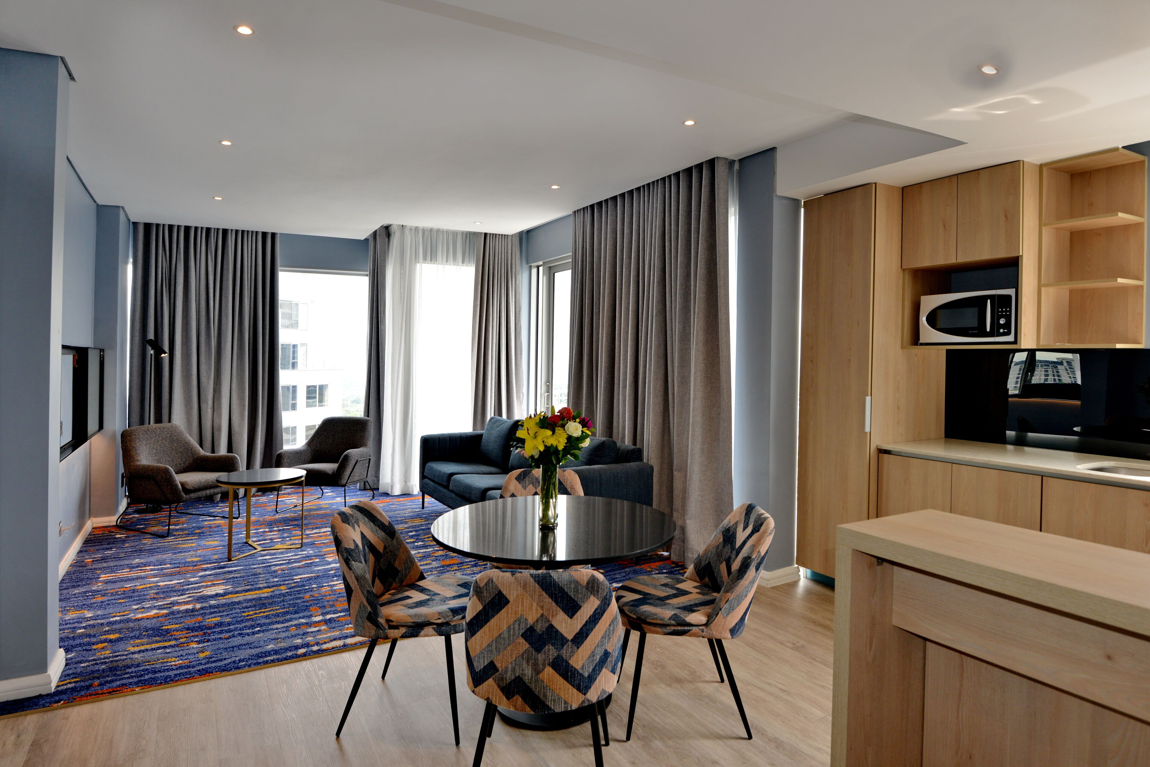 Una sala de estar moderna con una mesa redonda, dos sillones, un sofá y un ventanal con cortinas.