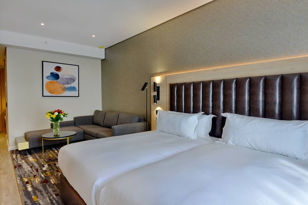 Een hotelkamer met een groot bed, een bank, een kleine tafel met een bloevas en een wandlamp.