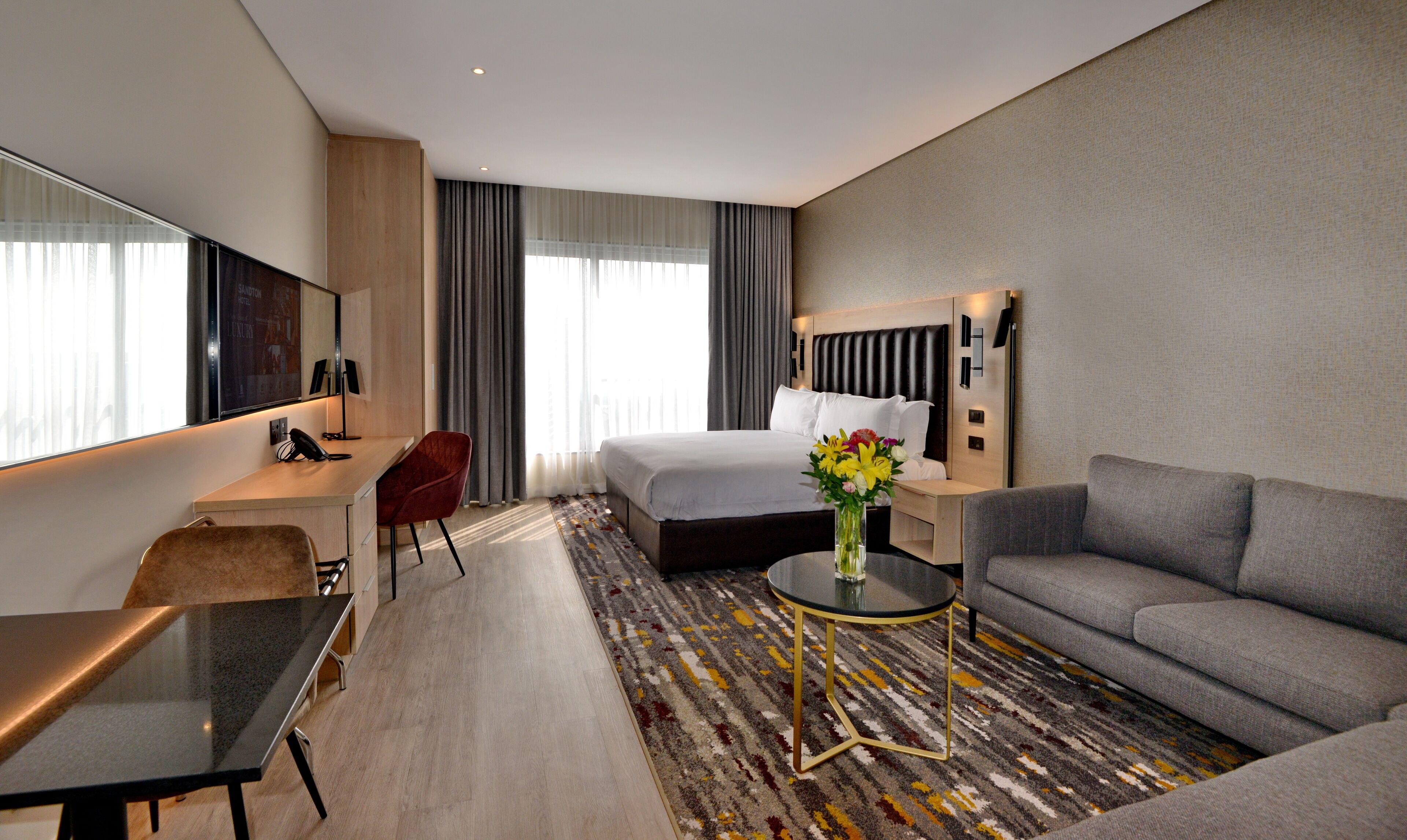 Una habitación de hotel moderna con una cama, un escritorio, una silla, un sofá y una mesita de centro.