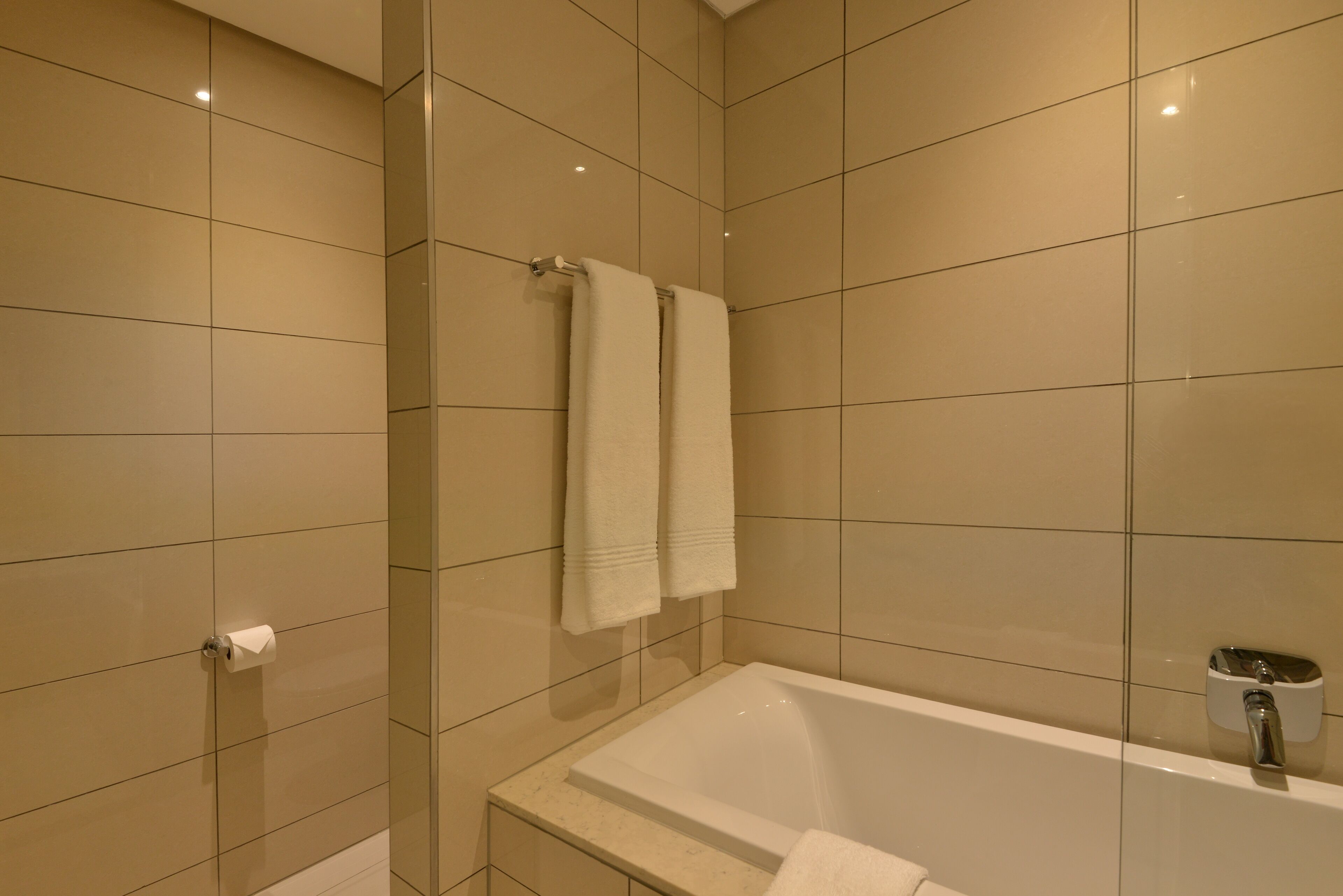 A modern bathroom with a bathtub, two towels hanging on a rack, and a toilet paper holder.