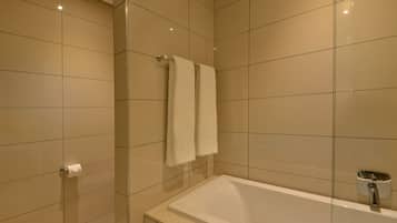 Un baño moderno con bañera, dos toallas colgadas en un perchero y un dispensador de papel higiénico.