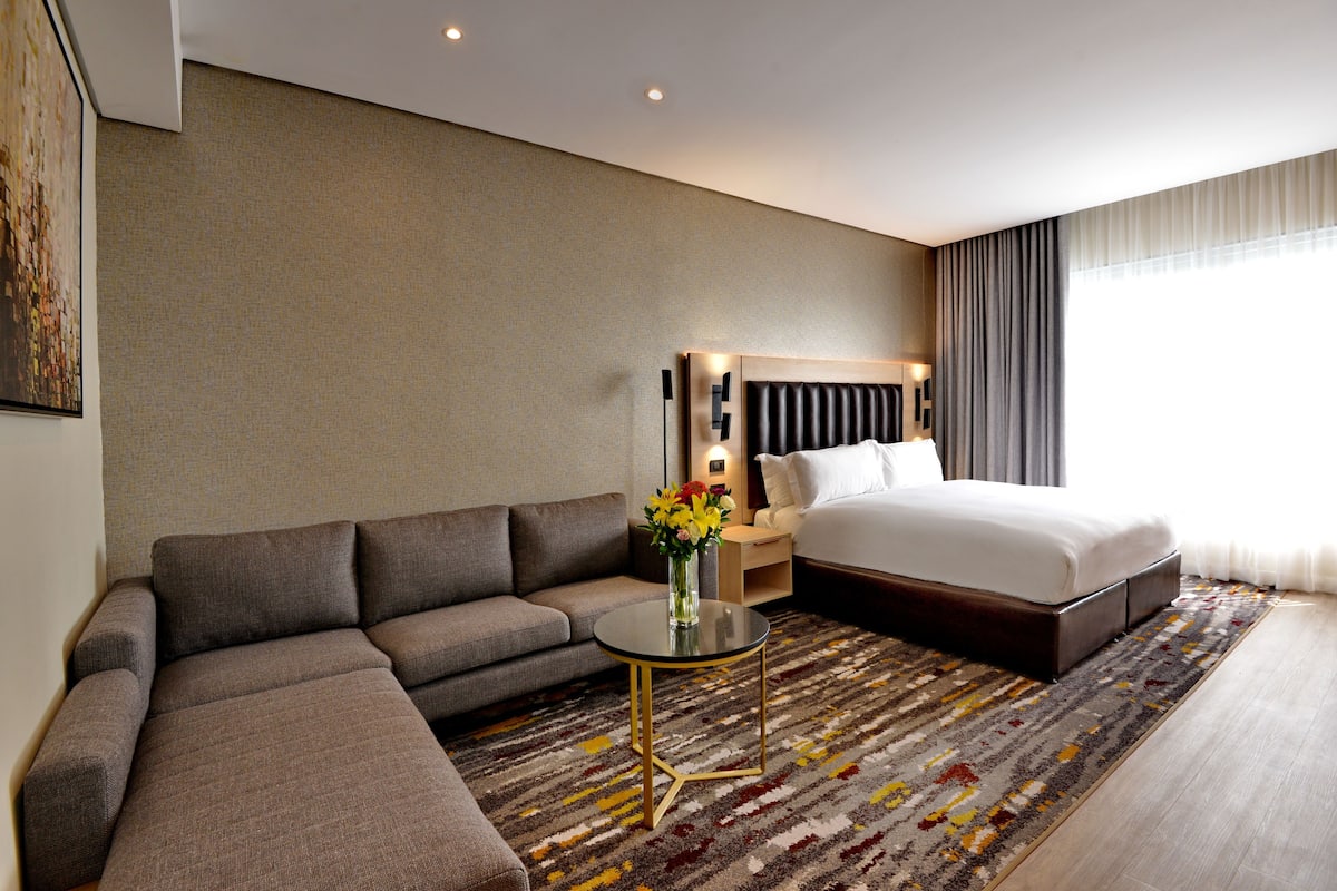 Een moderne hotelkamer met een groot bed, een sofa, een tafeltje en een decoratieve vaas.