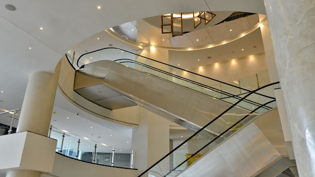 Un intérieur moderne avec des escaliers à volutes et des rampes de verre, comprenant un escalier mécanique central et plusieurs niveaux.