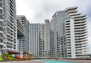 Um edifício residencial moderno e alto, com várias varandas e área de piscina.