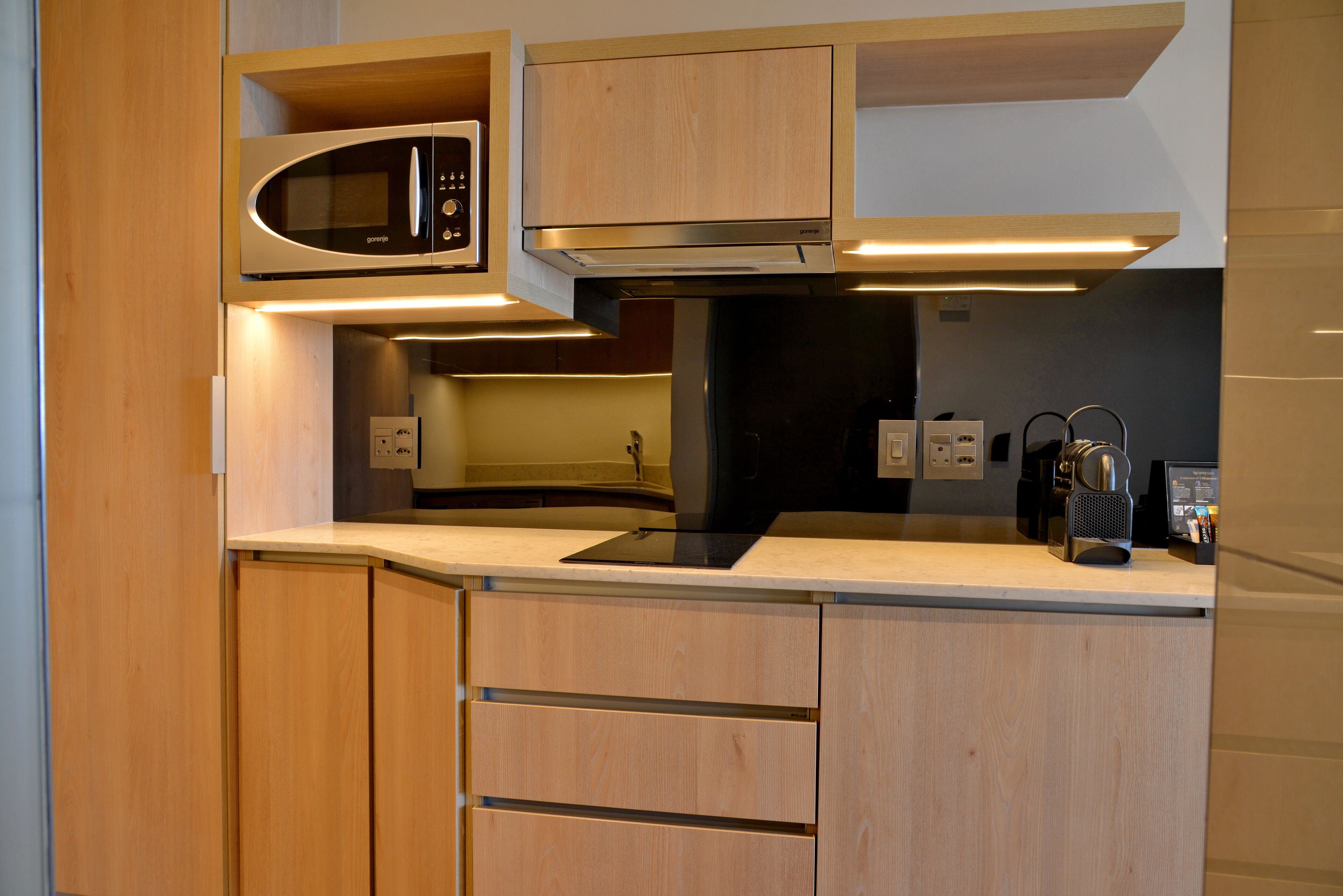 A modern kitchen with wooden cabinets, a built-in microwave, and a coffee machine.