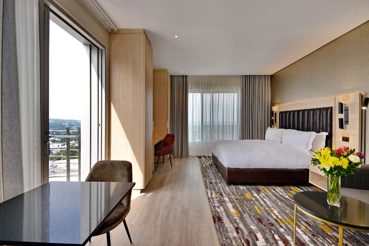Een hotelkamer met een groot bed, een bureau, een stoel en uitzicht op de stad.