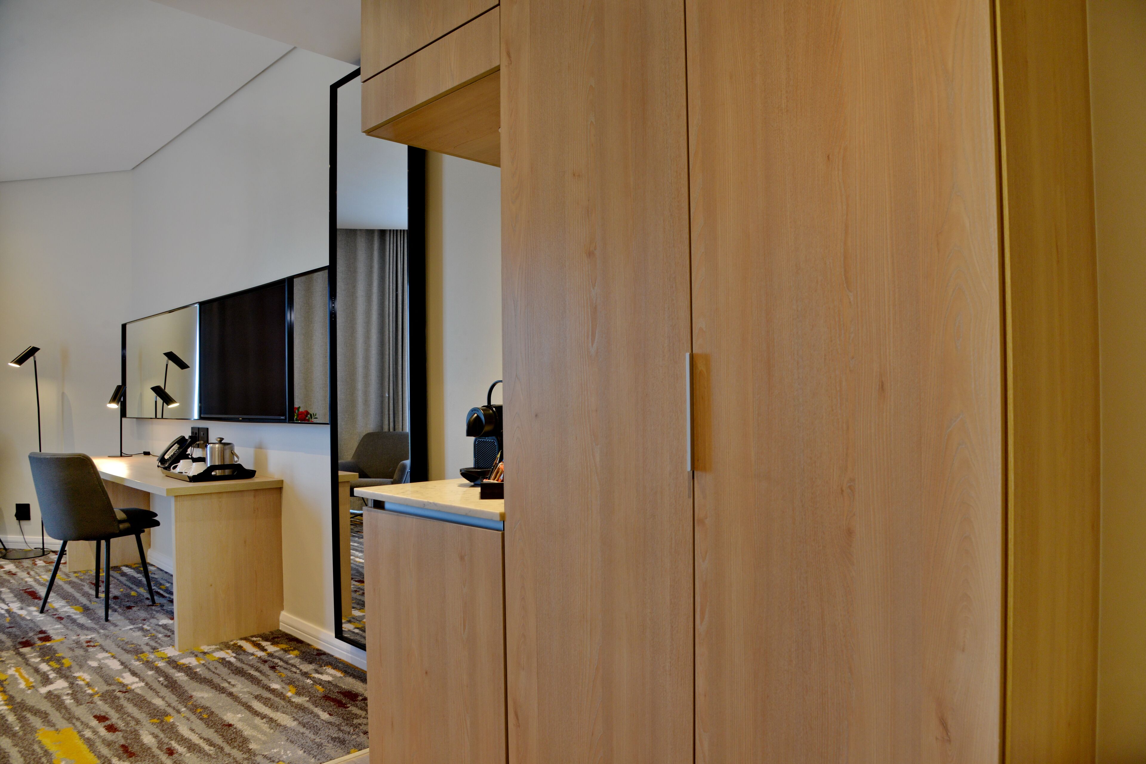 Una habitación de hotel con un escritorio de madera, una silla, un espejo y una cama.
