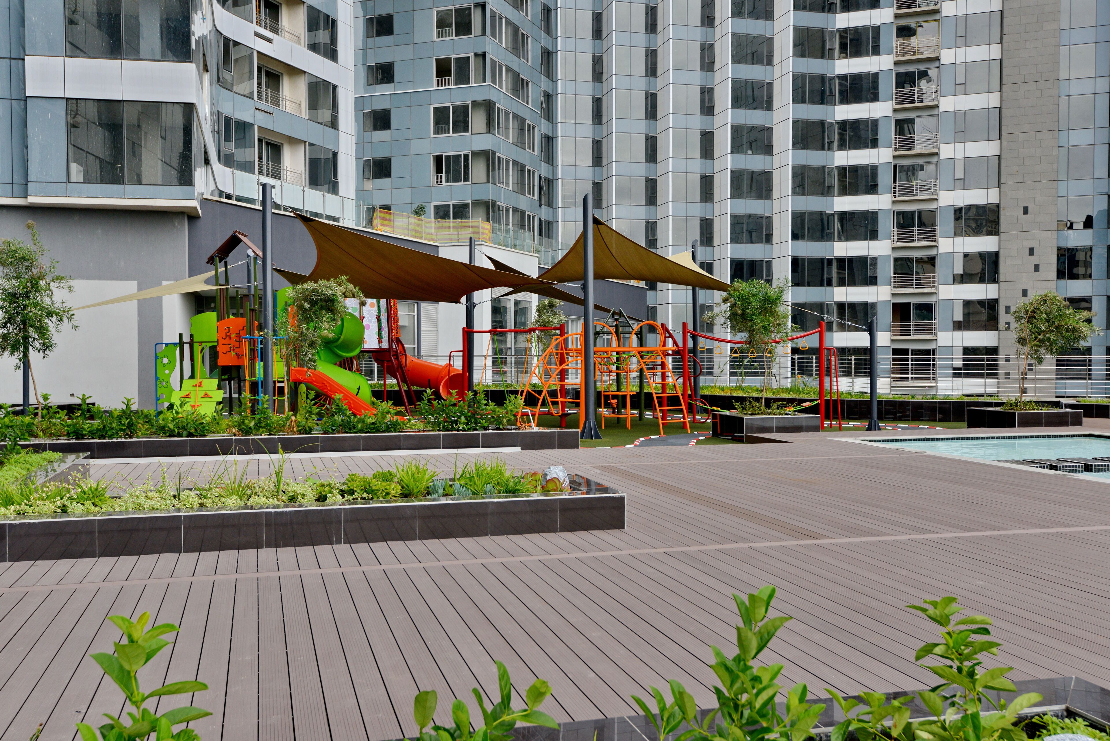 A playground with slides and climbing structures, surrounded by greenery and a wooden deck.