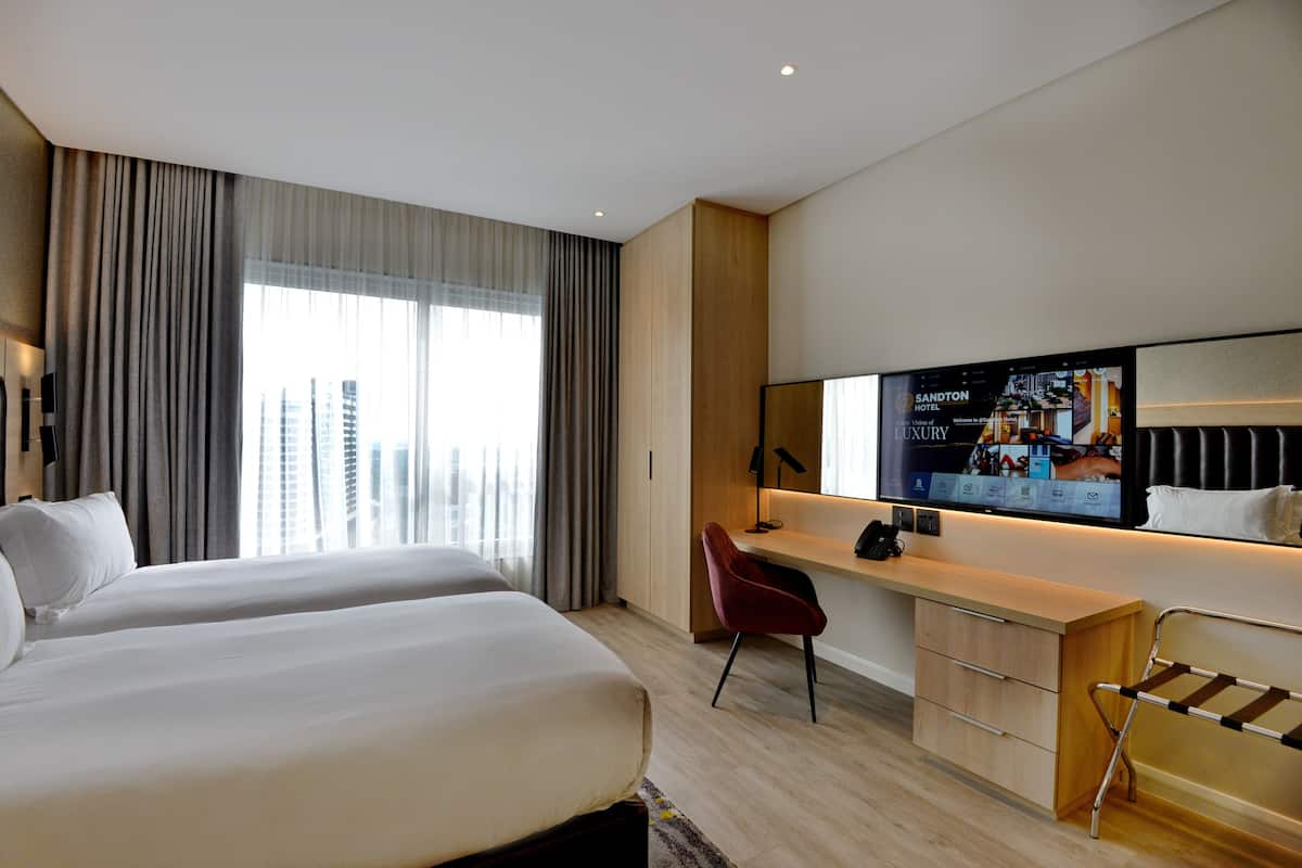 Een moderne hotelkamer met twee bedden, een bureau, een stoel en een groot televisiescherm.