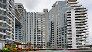 Un immeuble résidentiel moderne à plusieurs étages, doté de nombreux balcons, d’un jardin sur le toit et d’un espace piscine.