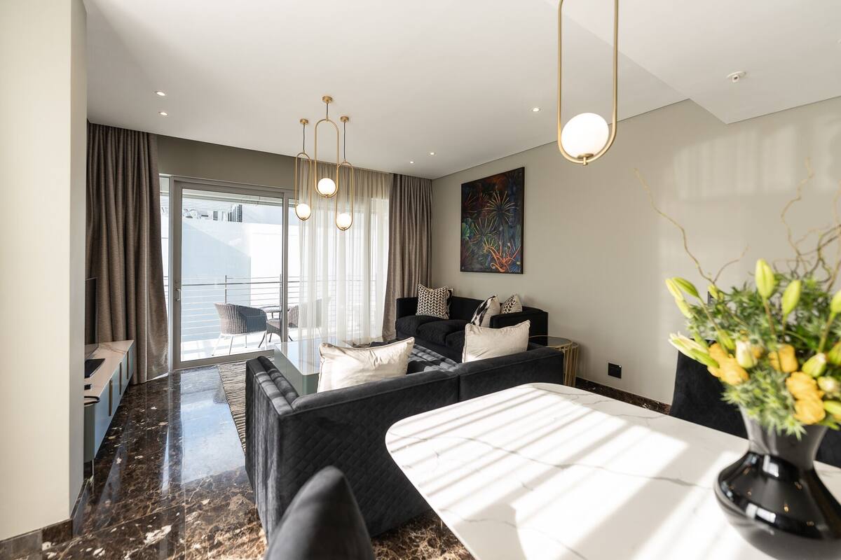 Een moderne woonkamer met een bank, een eettafel en een stadszicht door grote ramen.
