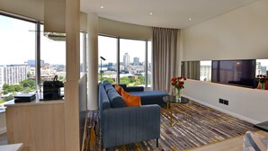 Une chambre d’hôtel moderne dotée d’une grande fenêtre donnant sur la ville, d’un canapé avec des coussins, d’une petite table sur laquelle est posé un vase, et d’un téléviseur à écran plat.