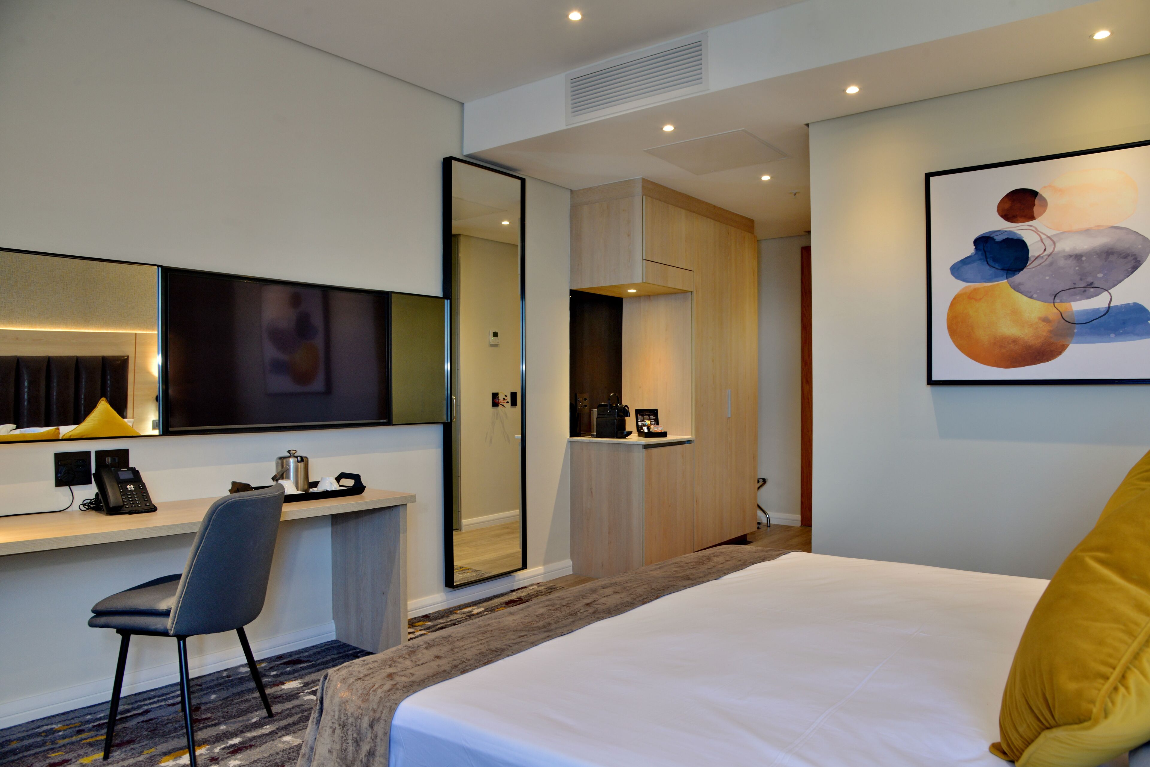 Een hotelkamer met een bed, een bureau met stoel, een spiegel, een schilderij en een kledingkast.
