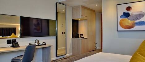 Une chambre d’hôtel comprenant un lit, un bureau avec une chaise, un miroir, un tableau et une armoire.