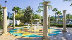A circular fountain with water jets surrounded by palm trees and columns.