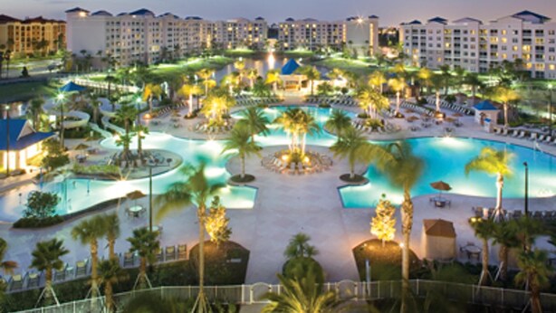 A resort with multiple swimming pools, palm trees, and a large building complex in the background.