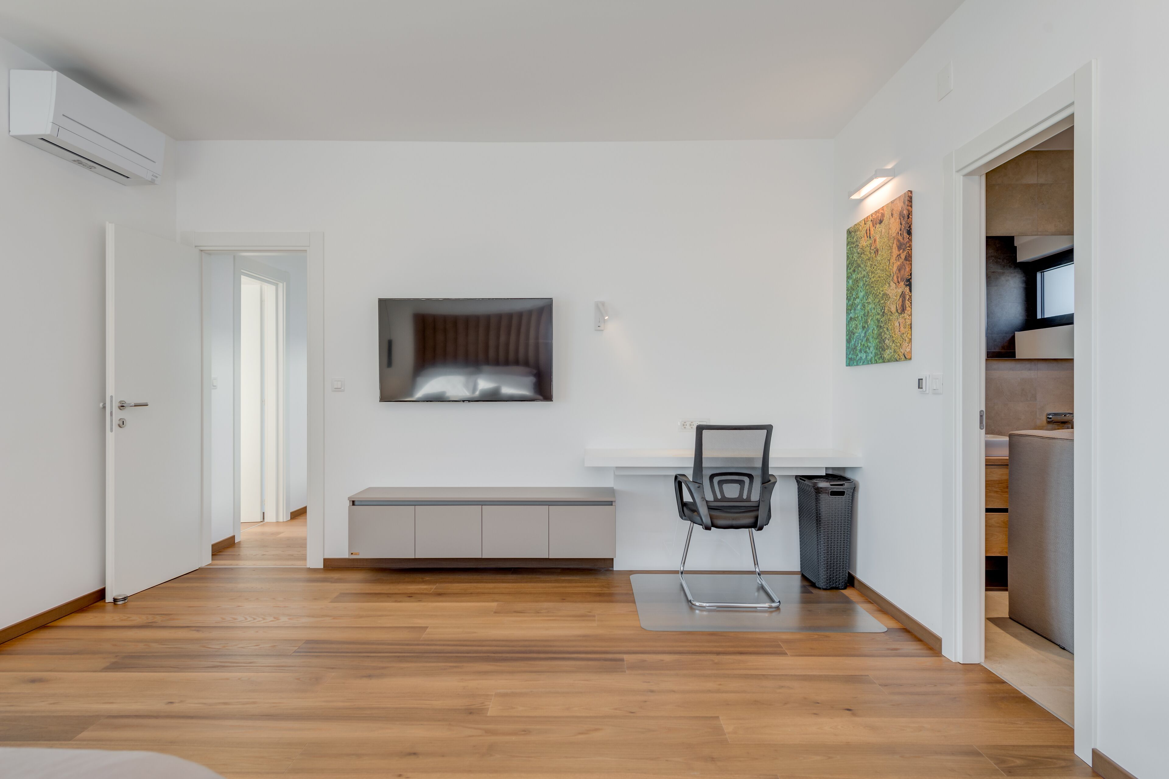 A modern, minimalist room with a wooden floor, a bench, a chair, and a trash bin.