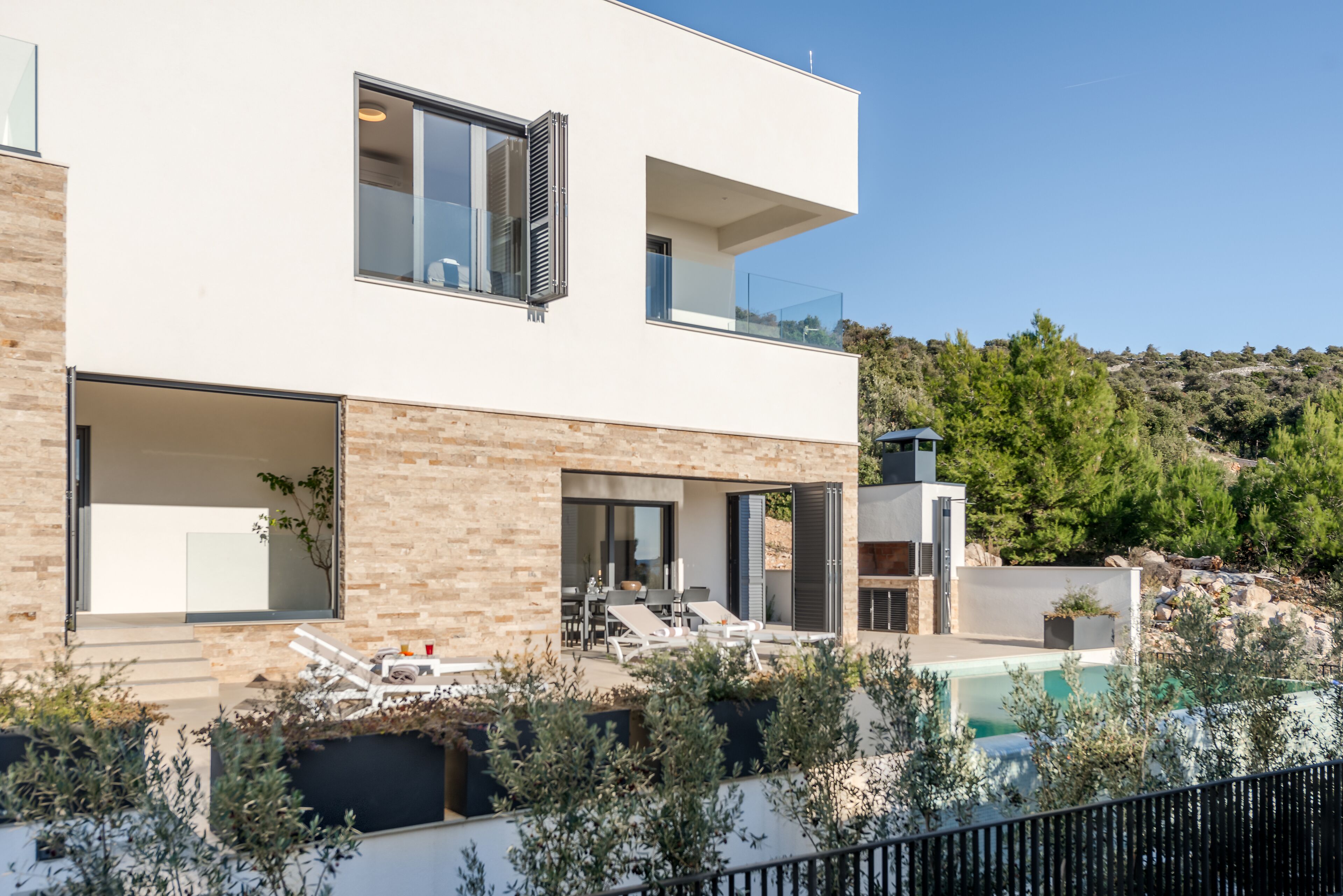 Une maison moderne à deux étages, dotée d’un balcon, d’une piscine et offrant une vue sur un paysage vallonné.