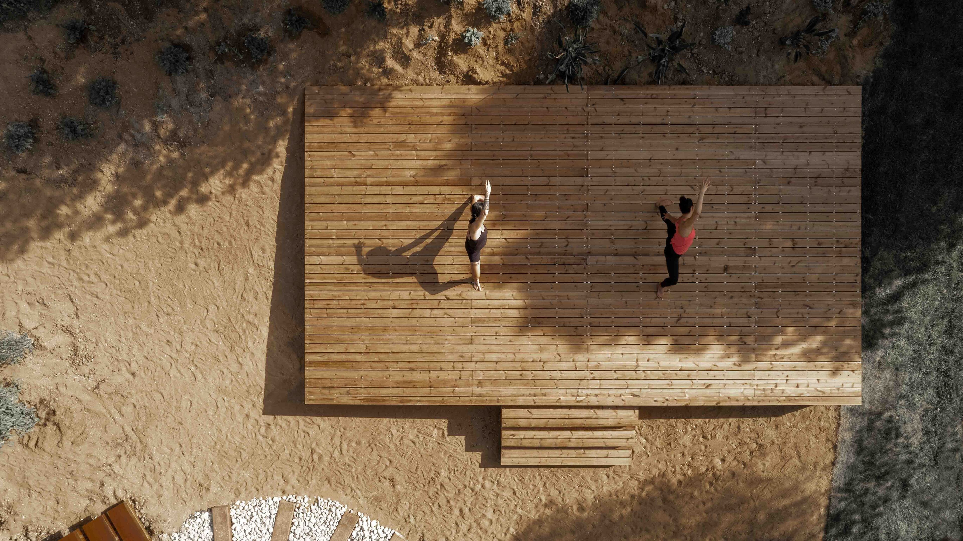 Vue aérienne d’une terrasse en bois où deux personnes pratiquent le yoga.