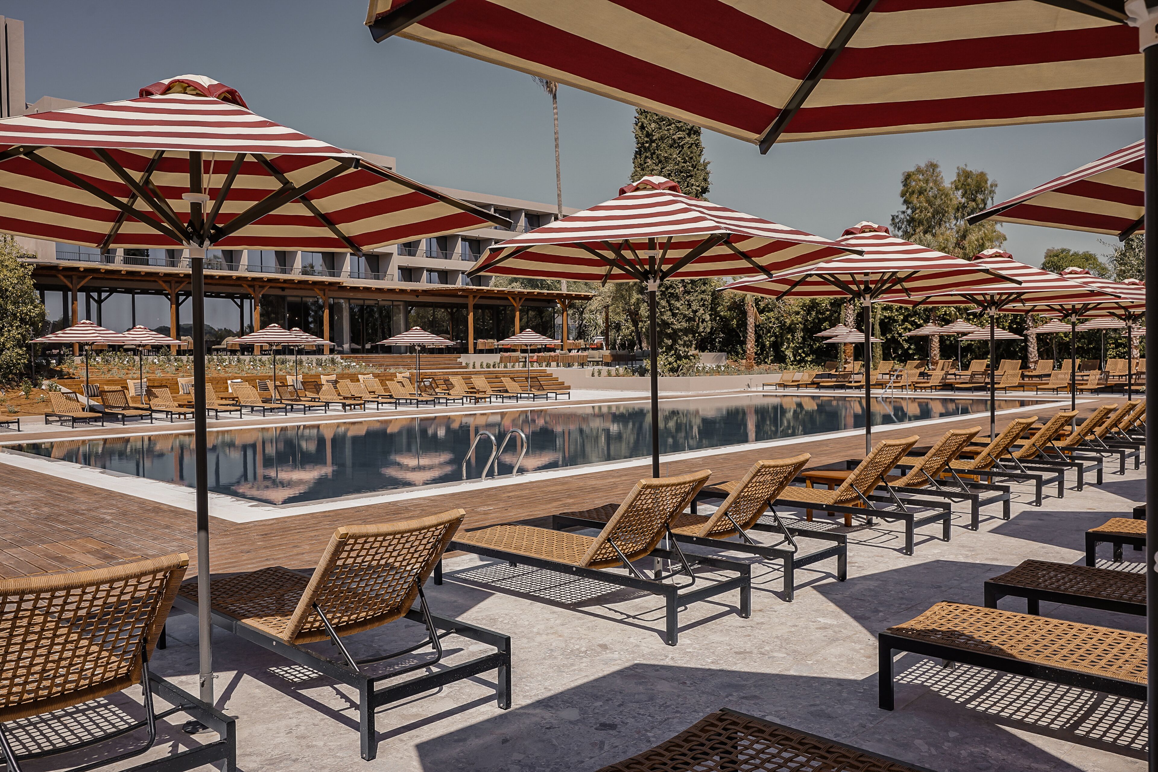 Un área junto a la piscina con sombrillas a rayas, sillas de descanso y una piscina reflejante.