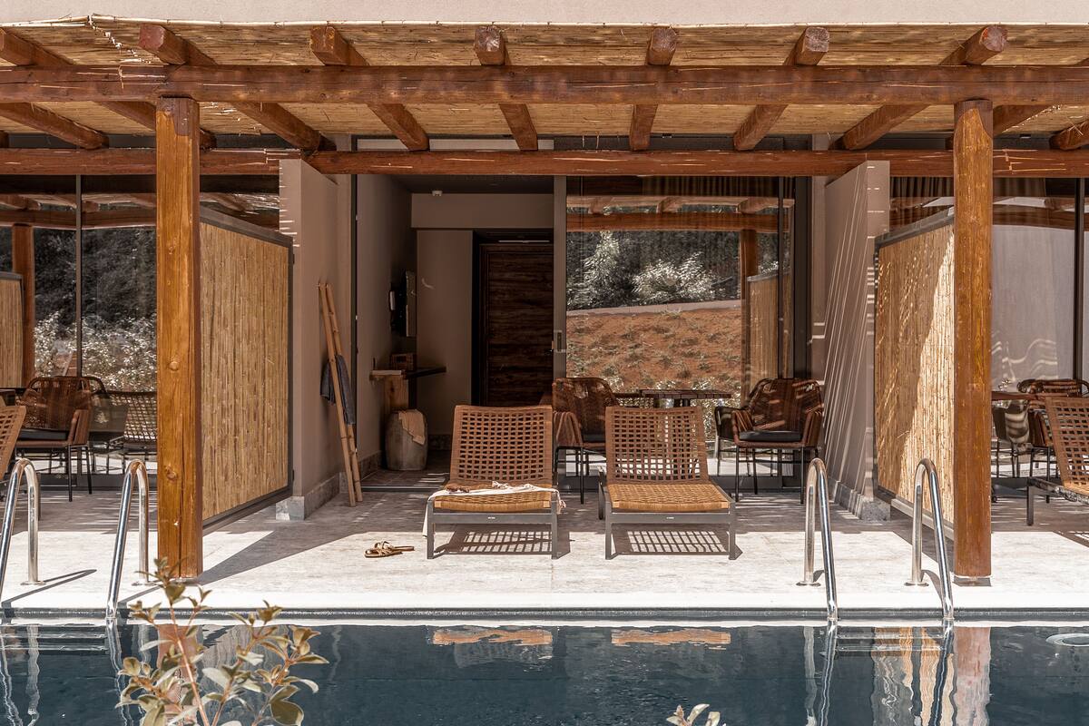 A poolside area with wooden pergolas, lounge chairs, and a clear view of the pool.