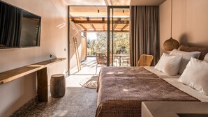 Ein modernes Schlafzimmer mit einem großen Bett, einem an der Wand befestigten Fernseher und einer Glastür, die zu einem Außenbereich mit Tisch und Stühlen führt.