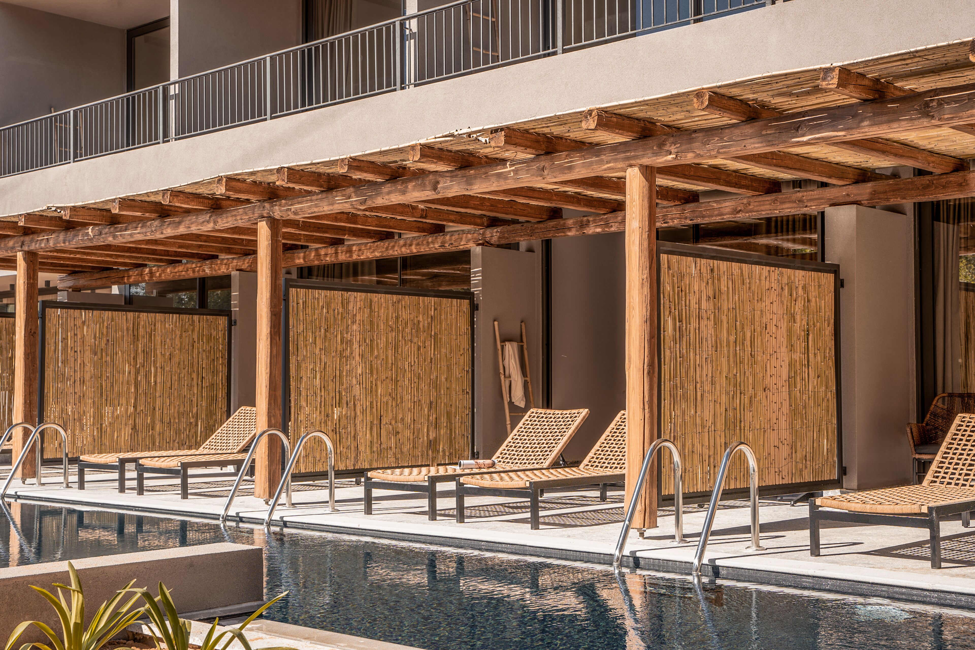 Un área de piscina con pérgolas de madera, sillones de descanso y una piscina cristalina.