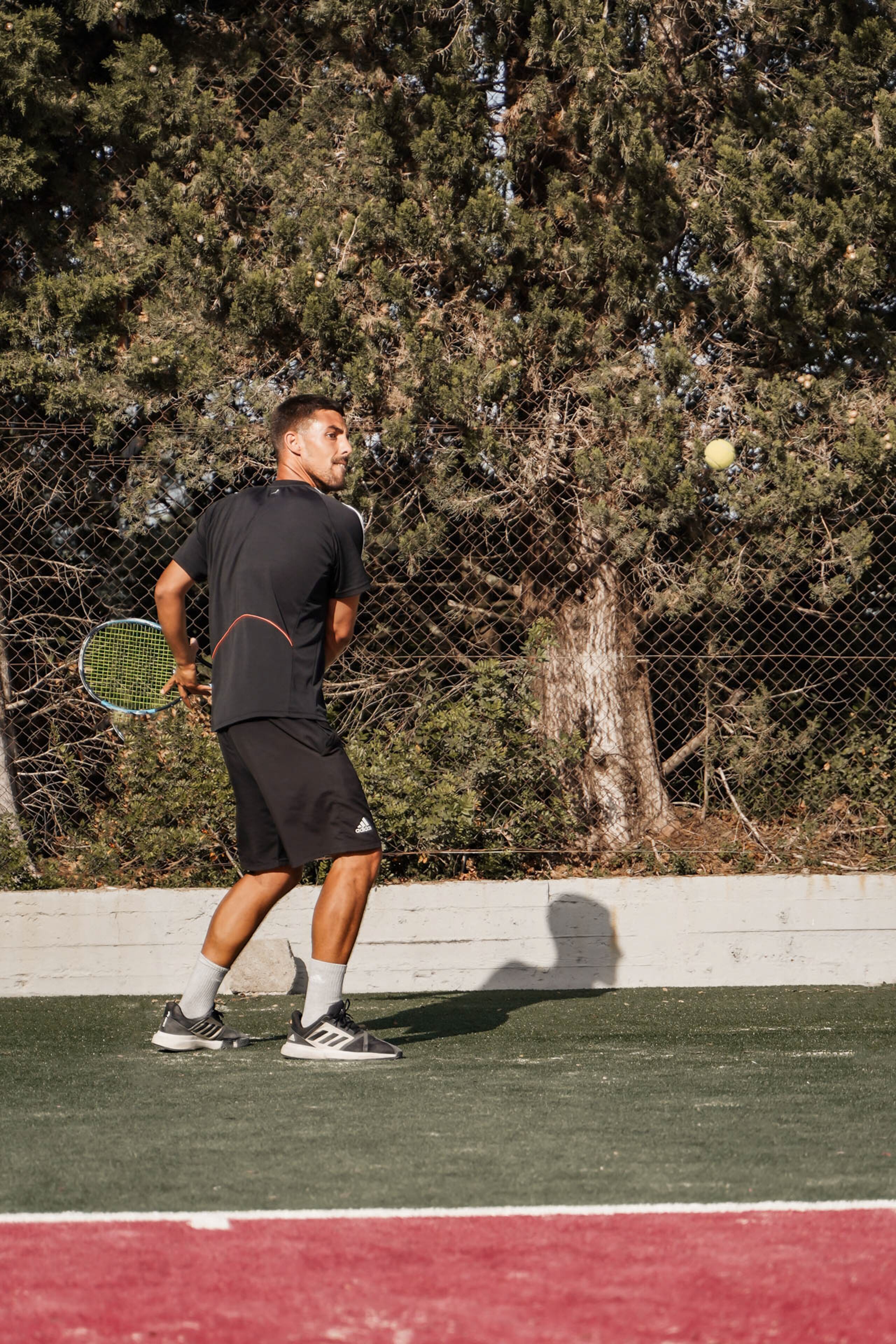 A tennis player on a court with a chain-link fence and trees in the background.
