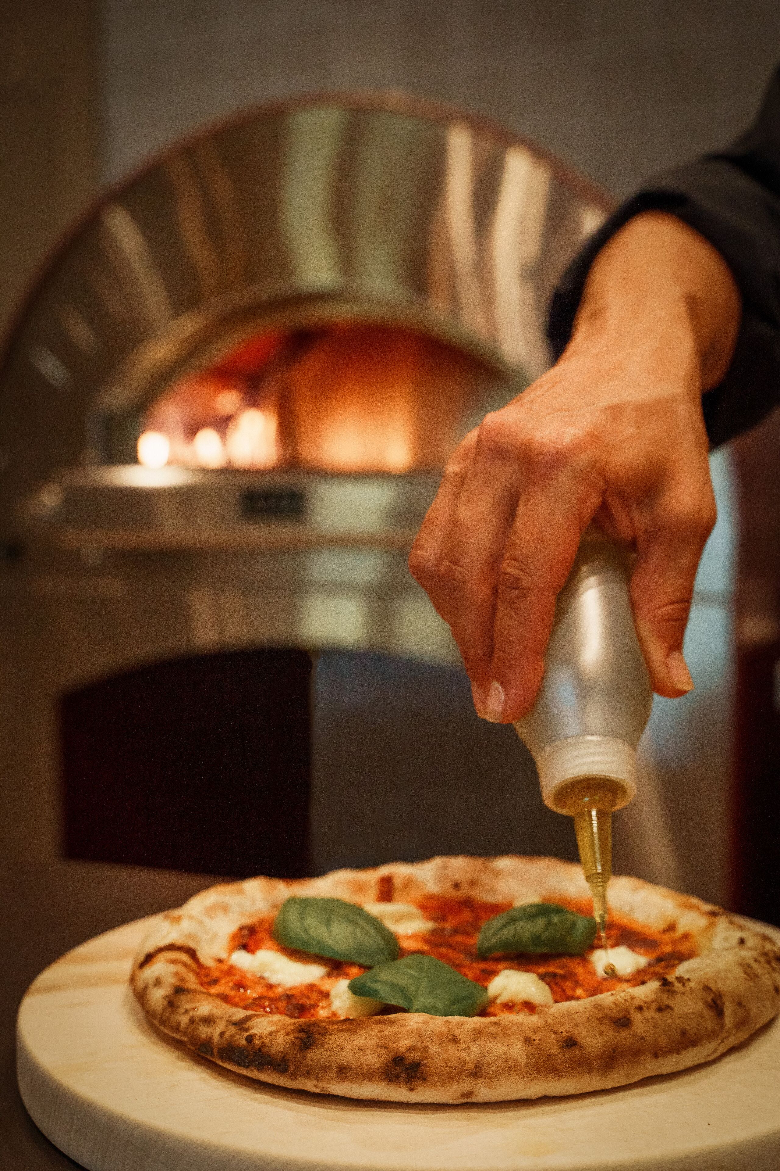 Una pizza preparándose, con una mano agregando salsa.