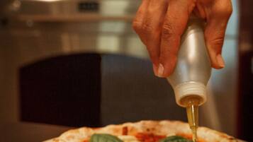 Una pizza preparándose, con una mano agregando salsa.