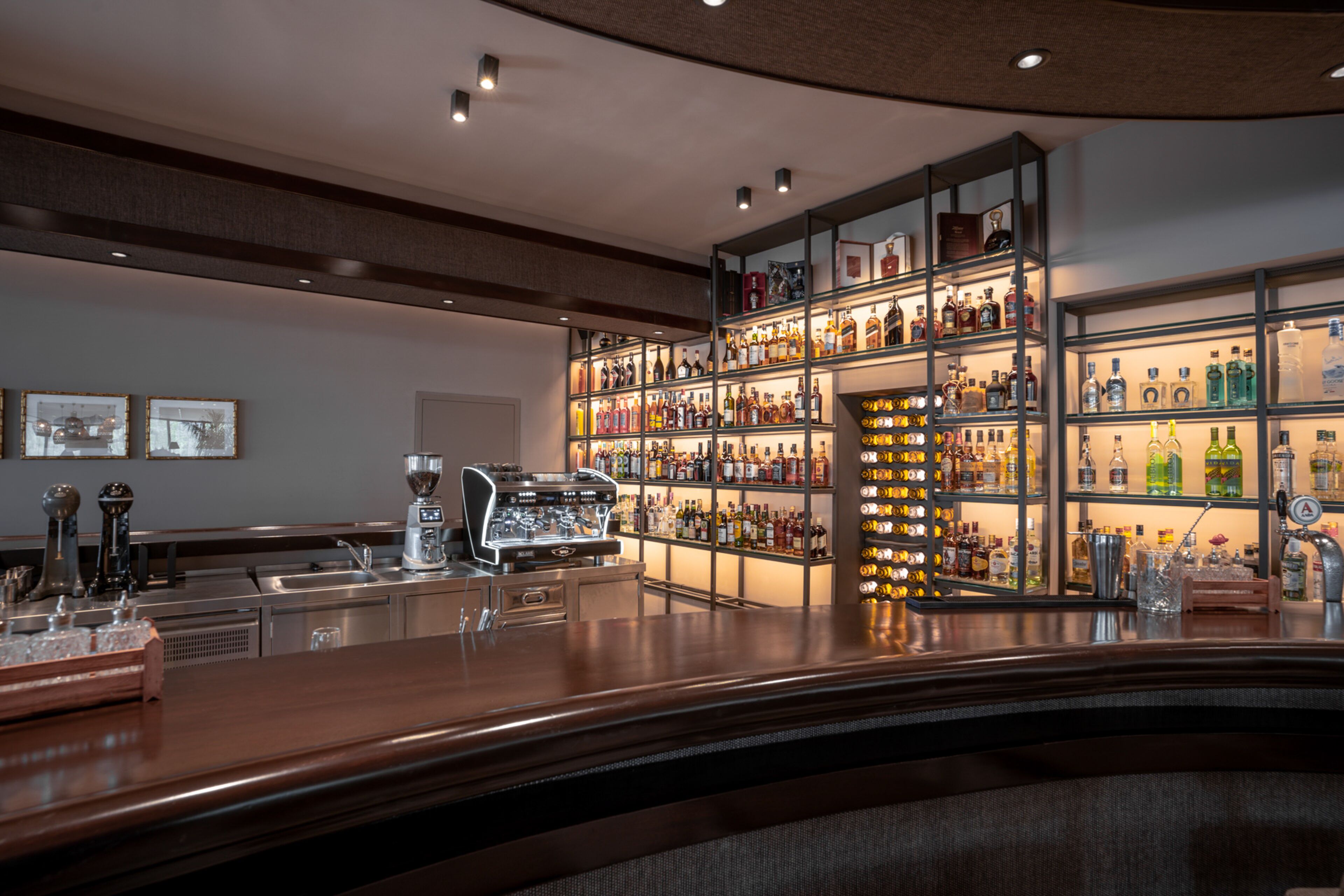 A bar area with a wooden counter, shelves of liquor bottles, and a coffee machine.
