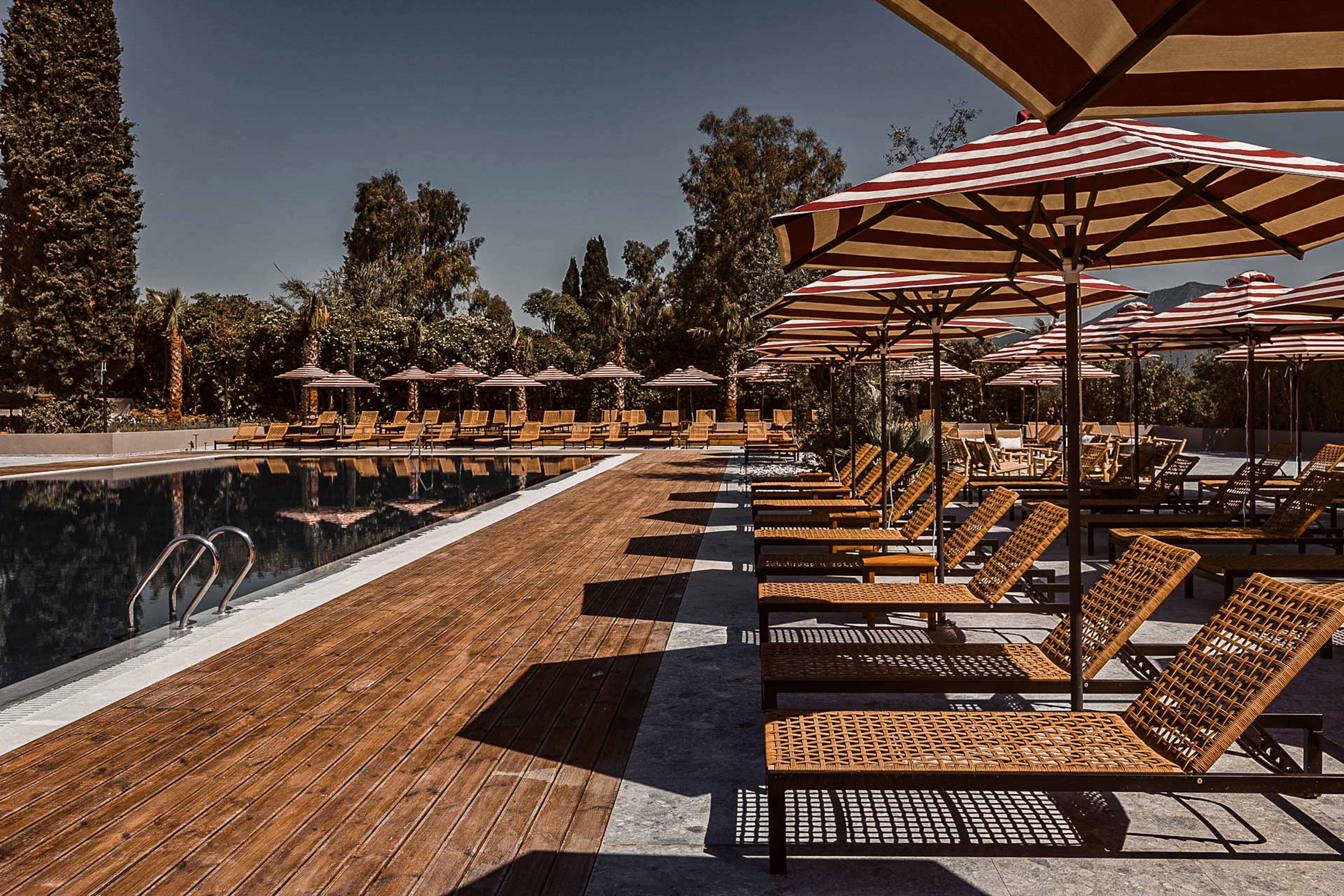 Un espace aménagé au bord de la piscine, avec une terrasse en bois, des chaises longues et des parasols à rayures.