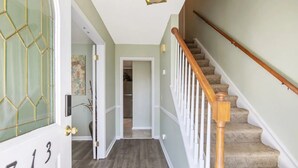 Un couloir avec un escalier en bois, une porte portant une plaque avec un numéro, et un luminaire au plafond.